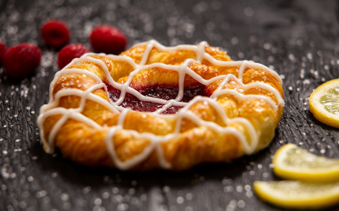 Little Rae's Bakery Lemon Raspberry Croissant on black wood with raspberries and lemons beside it.